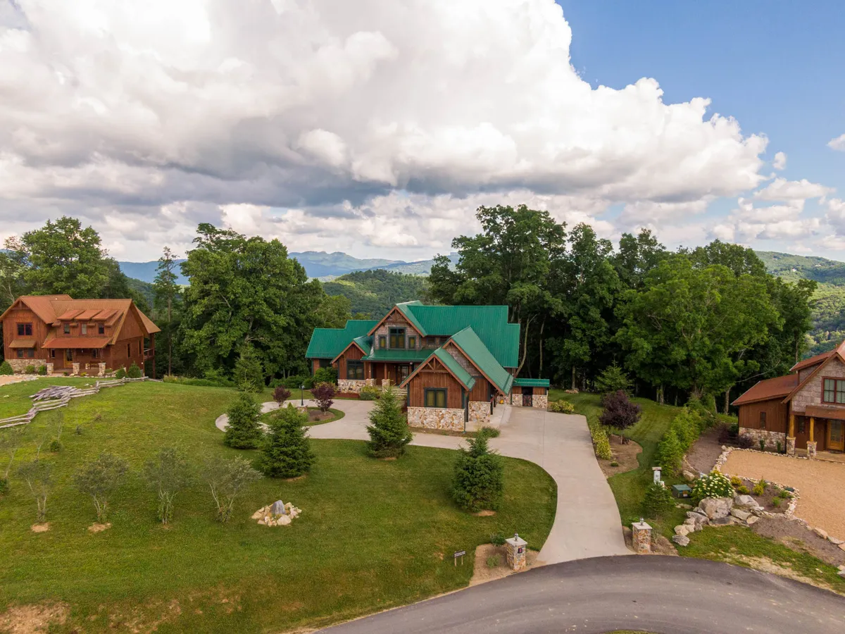 An inviting exterior view of the main house with a green roof, surrounded by trees and a well-kept yard. A neighboring cabin is visible, evoking a sense of community and the spaciousness offered by Eagles Nest. The setting conveys tranquility and opportunities for outdoor togetherness.