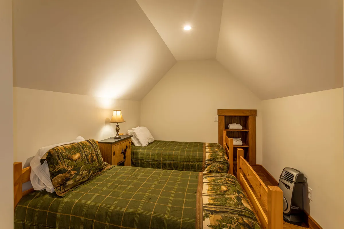 A cozy bunk room with a set of wooden bunk beds, a nightstand with a lamp, and a shelving unit. The inviting atmosphere is perfect for group sleepovers or family gatherings, with space for children or multiple guests.