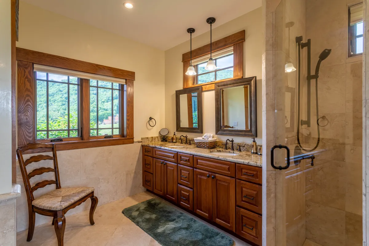 A bright, tranquil bathroom with a double-sink vanity, large mirrors, a walk-in shower, and a window revealing lush natural surroundings. The space is ideal for morning routines and offers a touch of luxury for guests.
