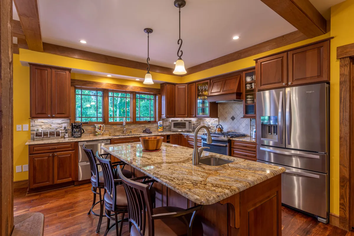The kitchen is featured with a central granite-topped island and bar stools, ample cabinetry, and large windows letting in natural light. The space is styled for family gatherings, cooking, and entertaining, with the island inviting guests to sit and mingle during meal prep.