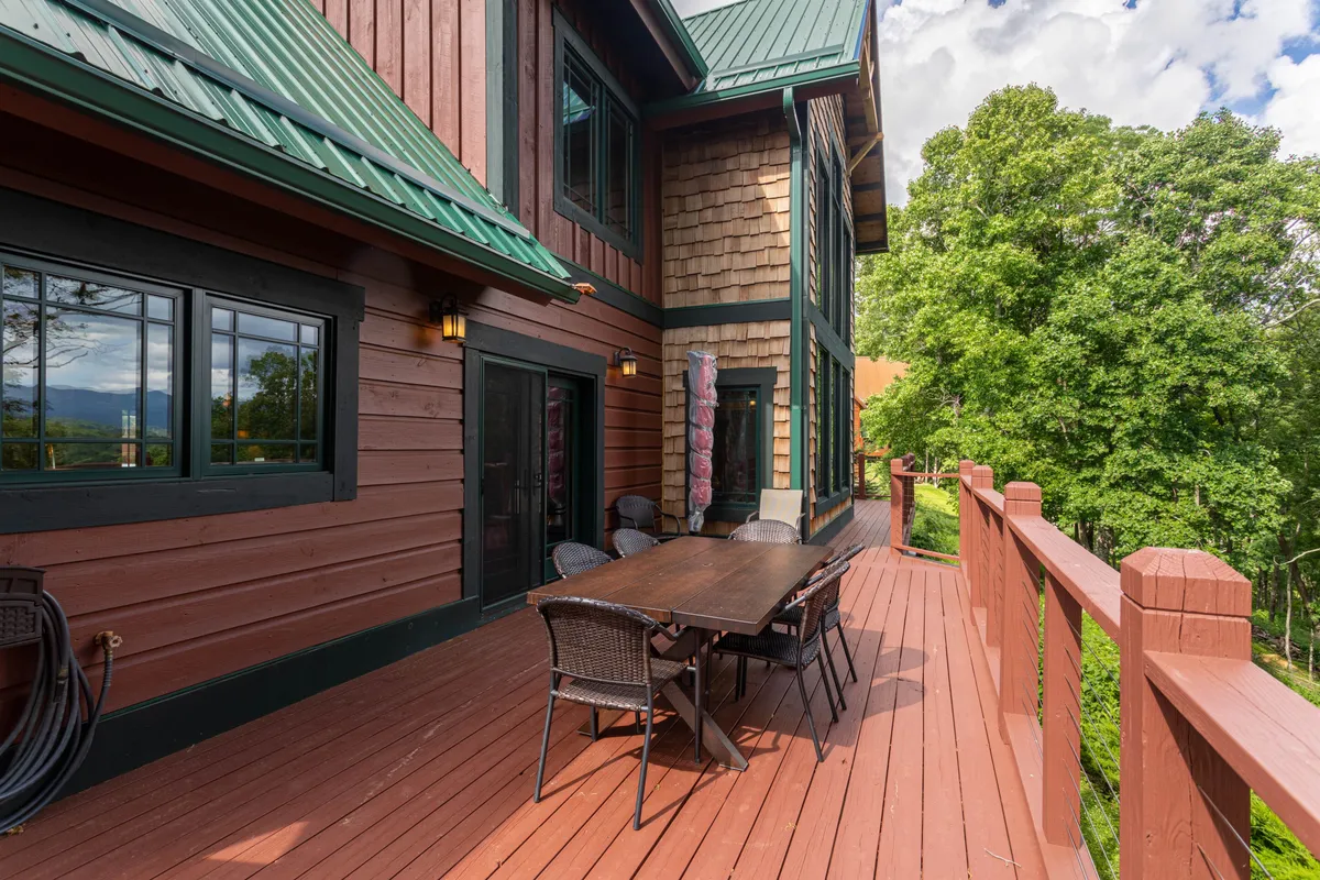 This exterior shot features comfortable deck furniture overlooking a scenic, tree-lined view, with a wooden railing framing the space. The setting radiates serenity, with hints of both daytime relaxation and nighttime stargazing possibilities.