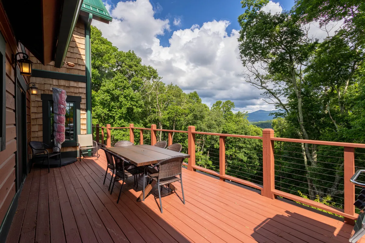 An outdoor dining area is set on a deck or patio, framed by trees and opening up to sweeping mountain vistas. The dining table is positioned to take full advantage of the natural scenery, ideal for meals with family or friends while immersed in nature.