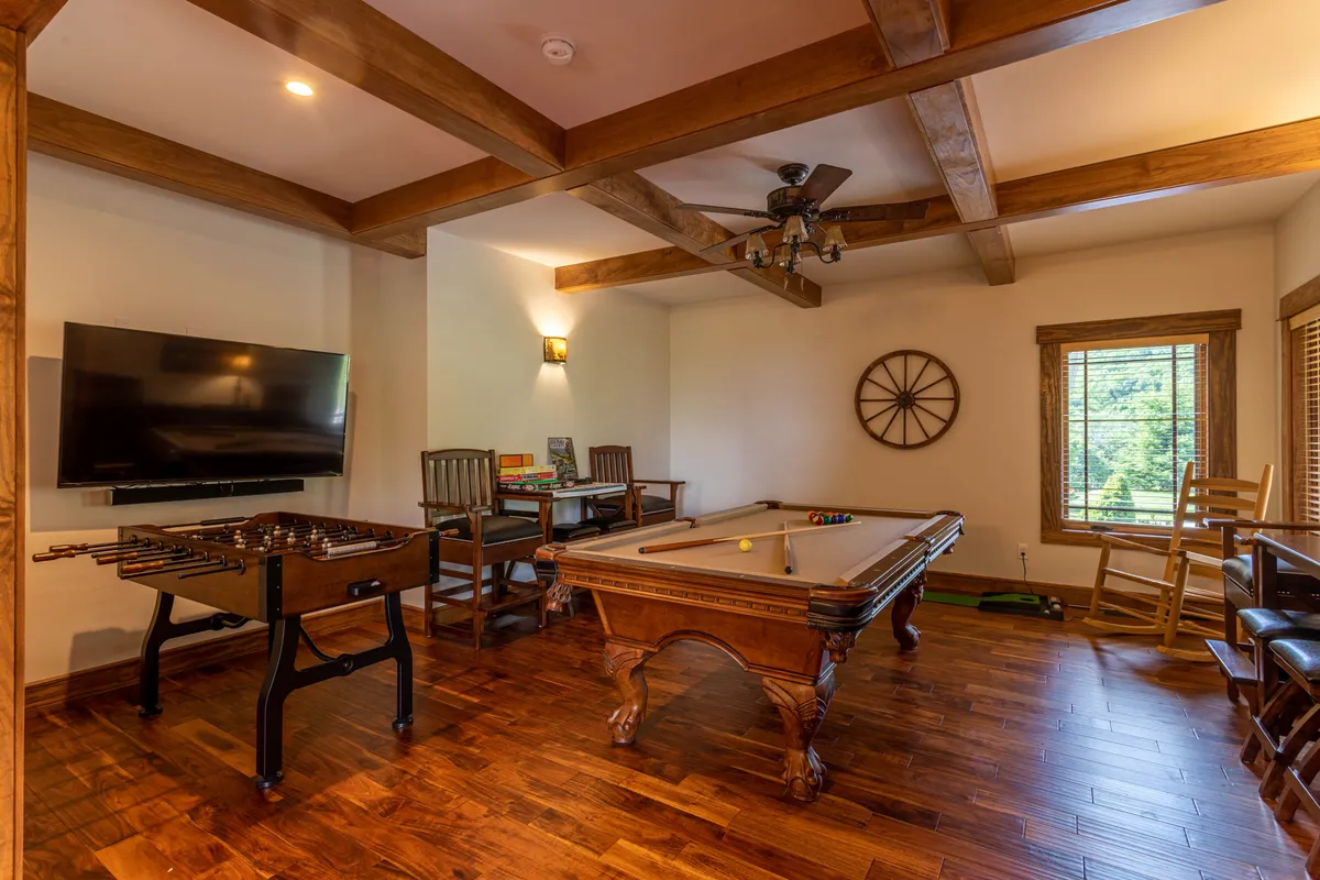 This image showcases a vibrant game room featuring a pool table, foosball table, a wall-mounted TV with a soundbar, comfortable wooden furniture, and a window that brings in natural light. The space is inviting, designed for group activities and socializing, and visually highlights the playful, family-friendly atmosphere described in the section.